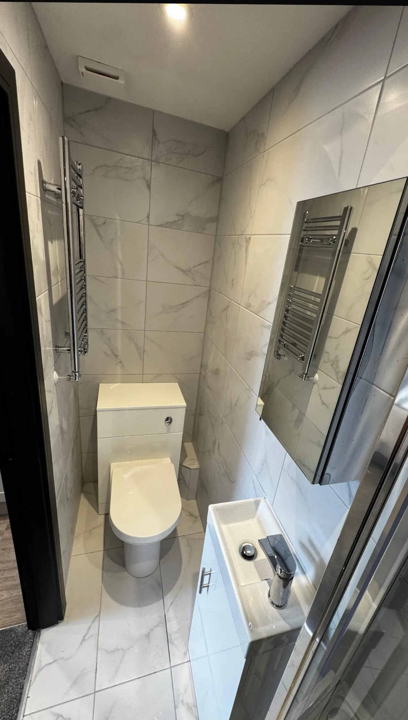 A finished en-suite shower room with marble-effect tiling, a heated towel rail and a glass screen