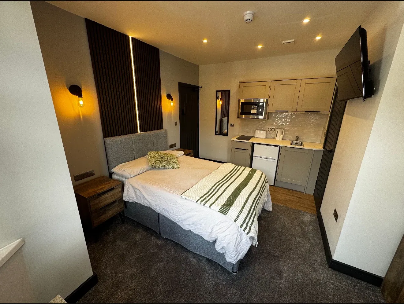 A finished studio-style letting room at Albert Street, with a fitted kitchenette, slatted feature wall and wall lights