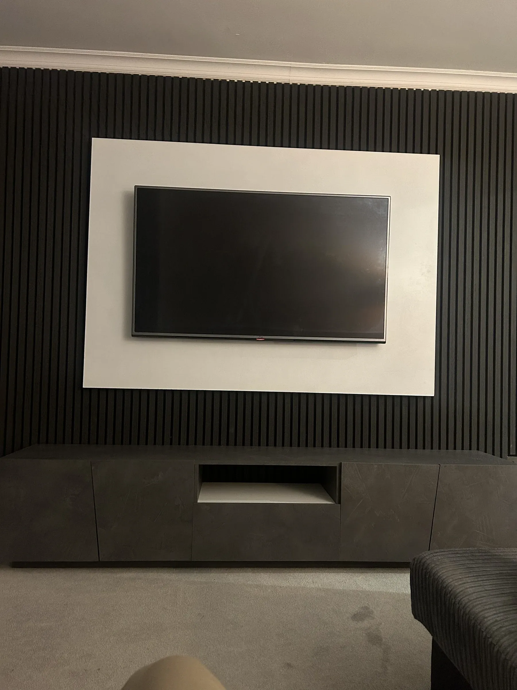 A finished communal living space with a slatted charcoal feature wall, wall-mounted television and built-in bench seating