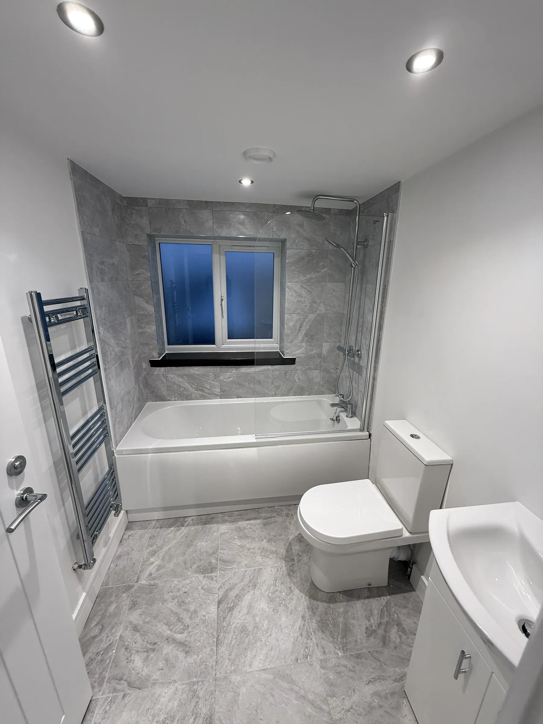 The finished bathroom with a bath and shower over, marble-effect panelling and a heated towel rail