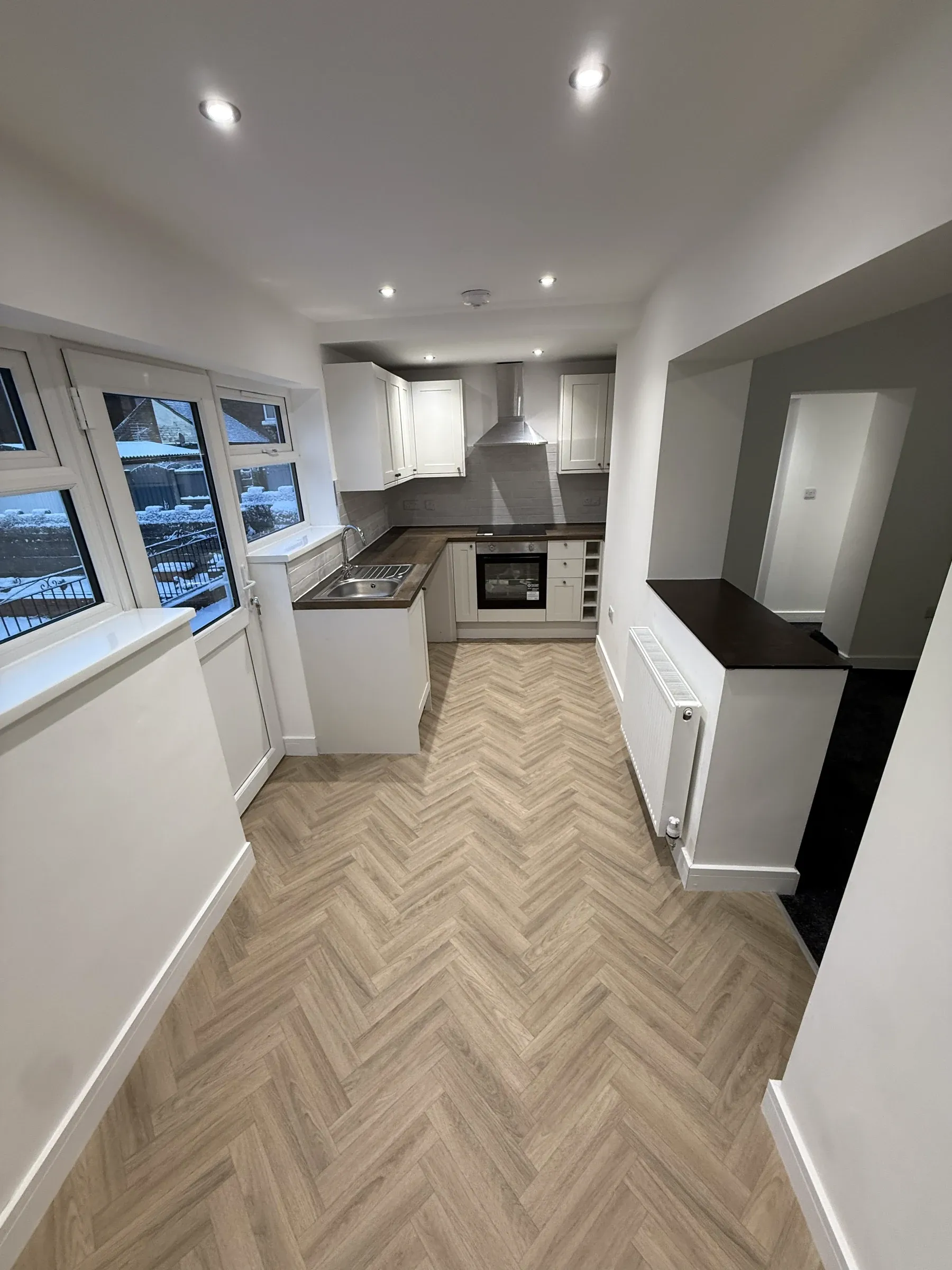The finished kitchen in a buy-to-let refurbishment, with white units, dark worktops and herringbone flooring