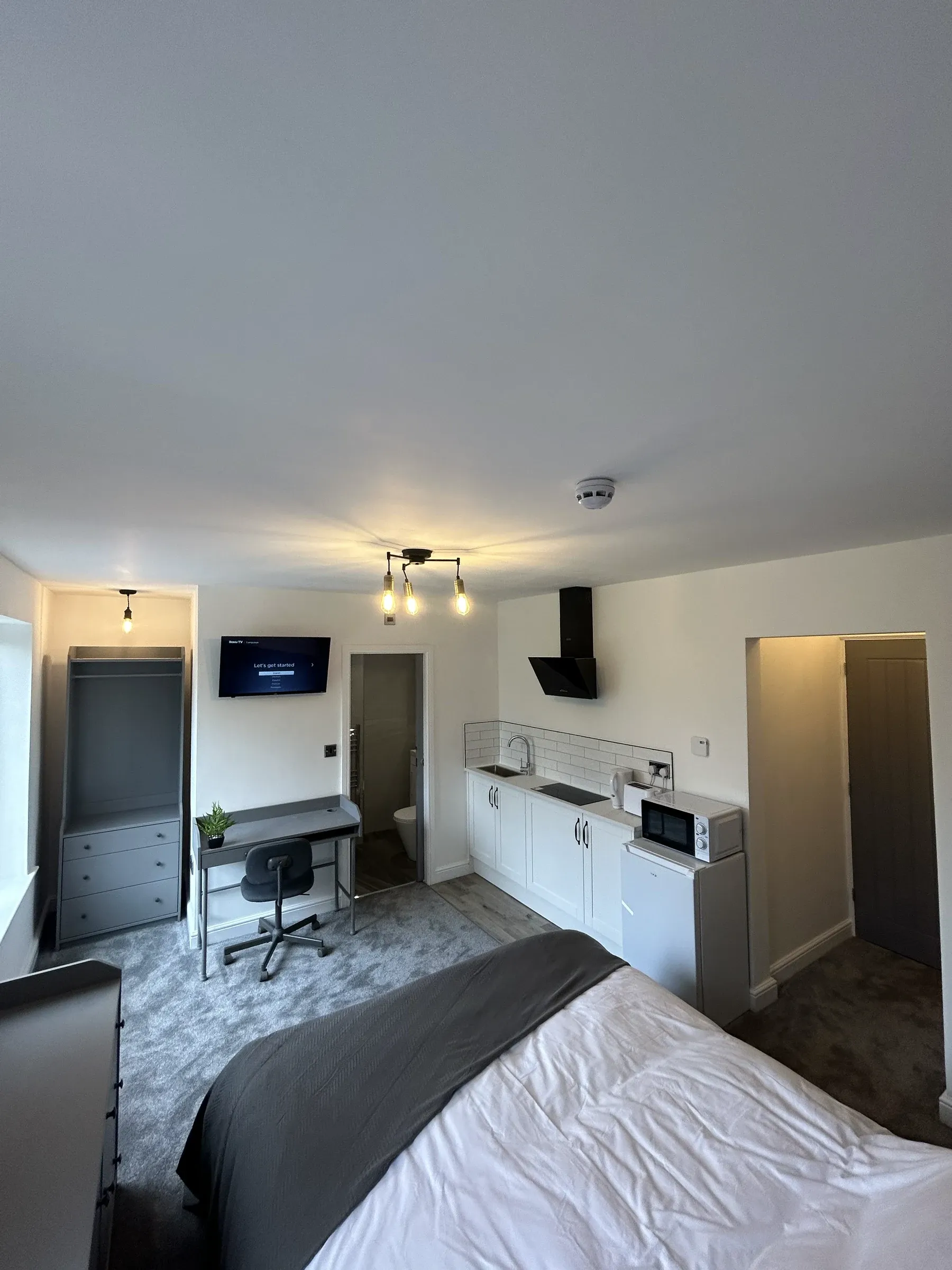 A finished letting room with a double bed, desk, wall-mounted television and fitted kitchenette