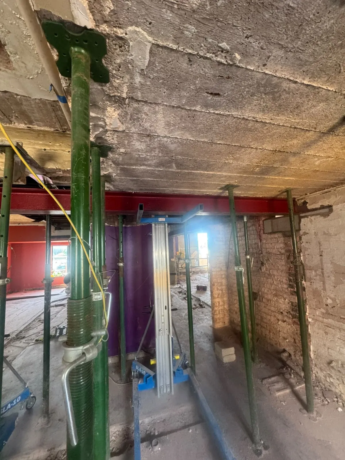 Adjustable steel props supporting a ceiling with a red steel beam installed above