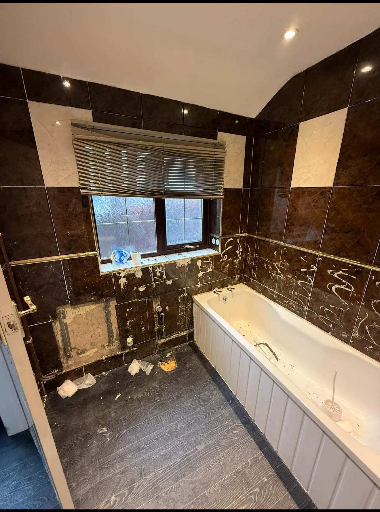 The original bathroom before work started — dark brown and gold tiling, tiles stripped off the wall and debris on the floor