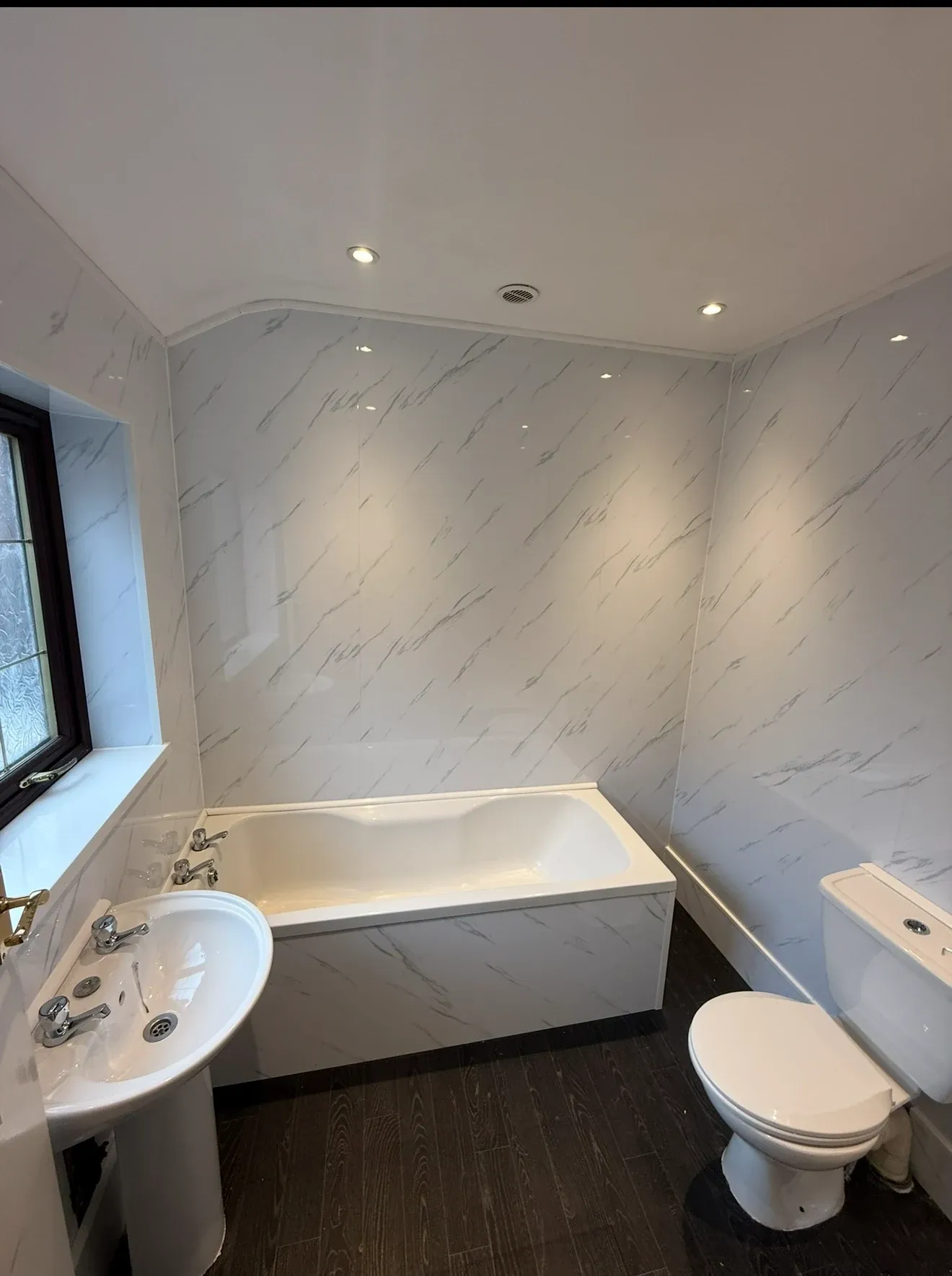 The same bathroom finished, with white marble-effect panelling, a new bath, basin and WC