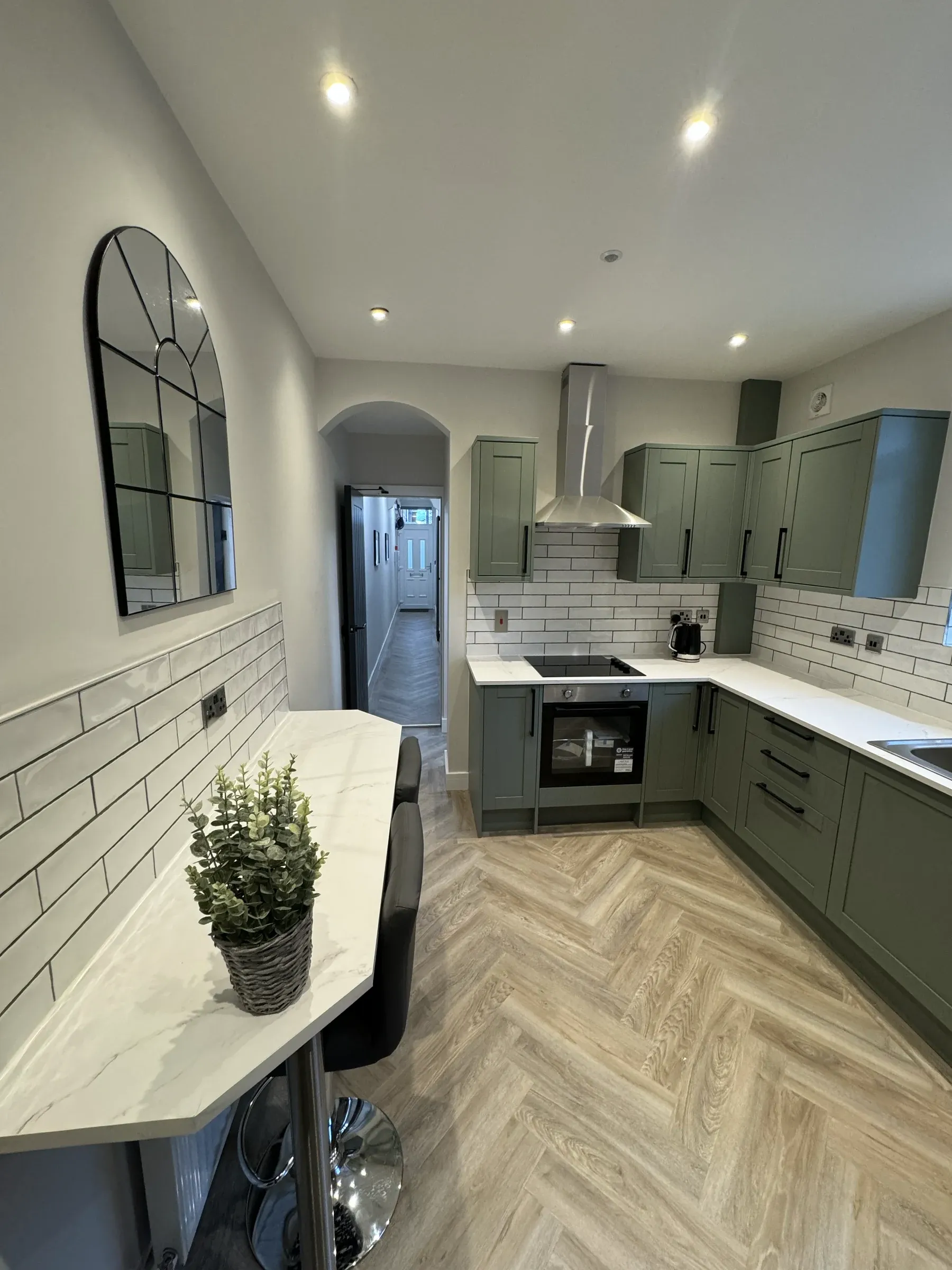 A finished communal kitchen with a breakfast bar, olive green units and herringbone flooring