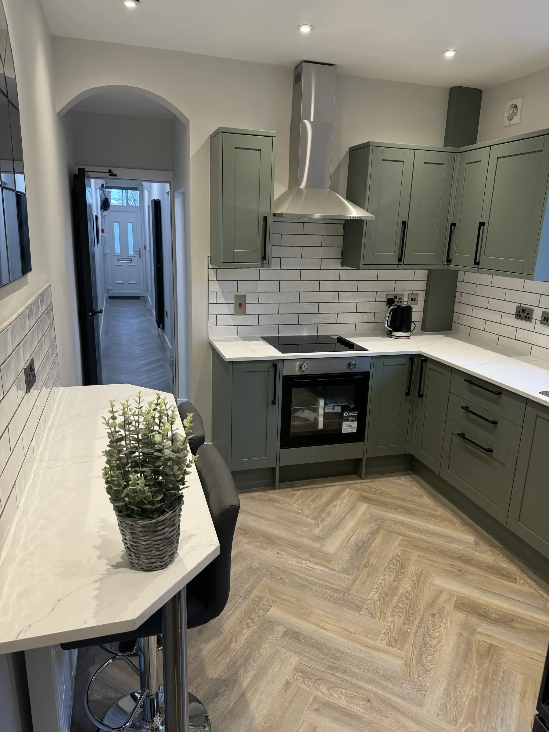 A finished kitchen with olive green shaker units, metro tiling and herringbone flooring