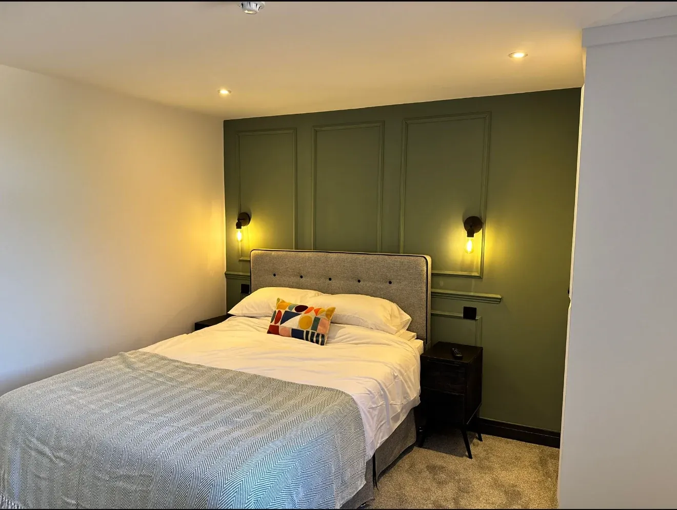 A finished letting room at 28 Oxford Road, with a green panelled wall and wall lights either side of the bed