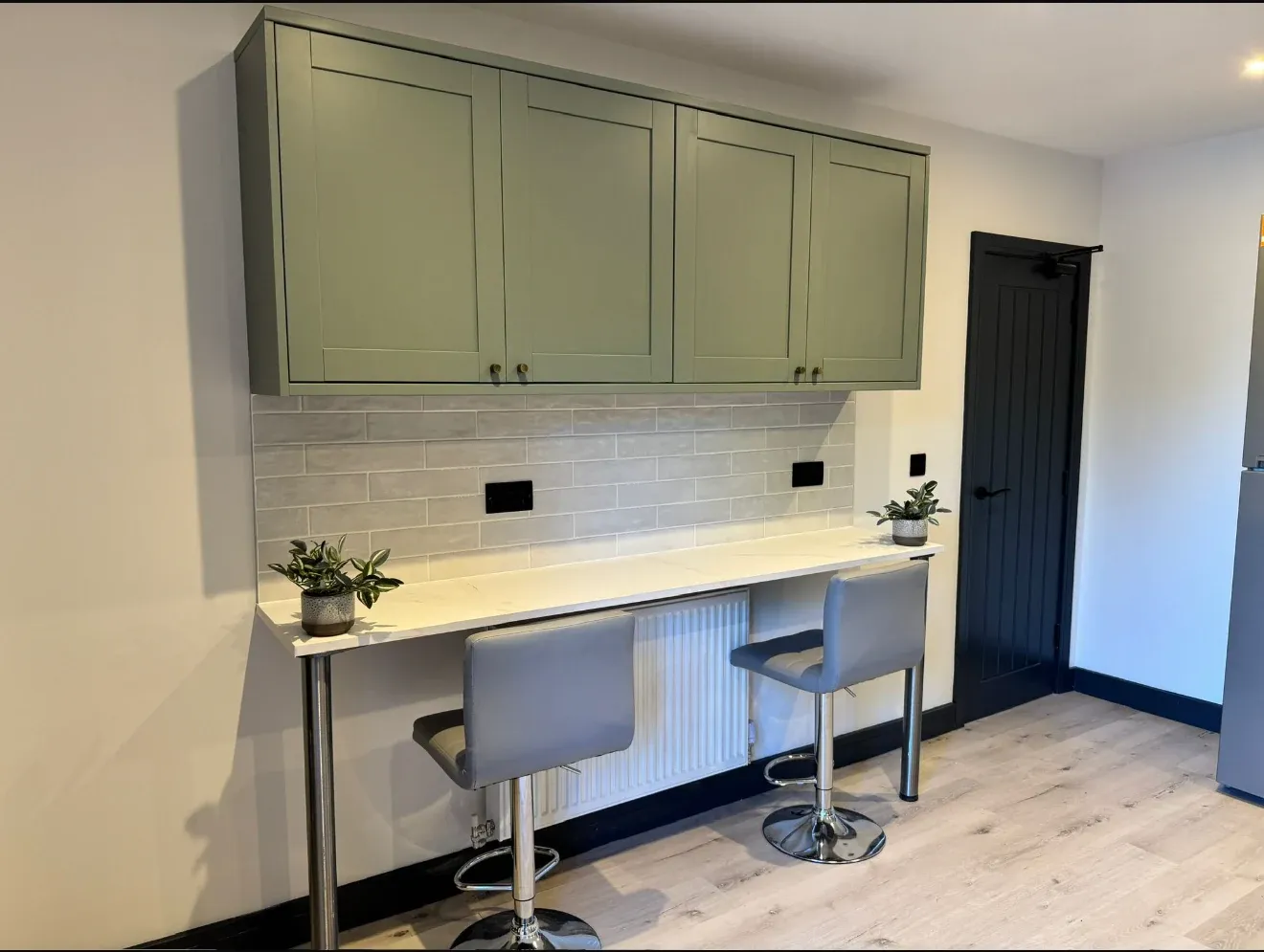 A breakfast bar with two stools built along the kitchen wall, under wall units