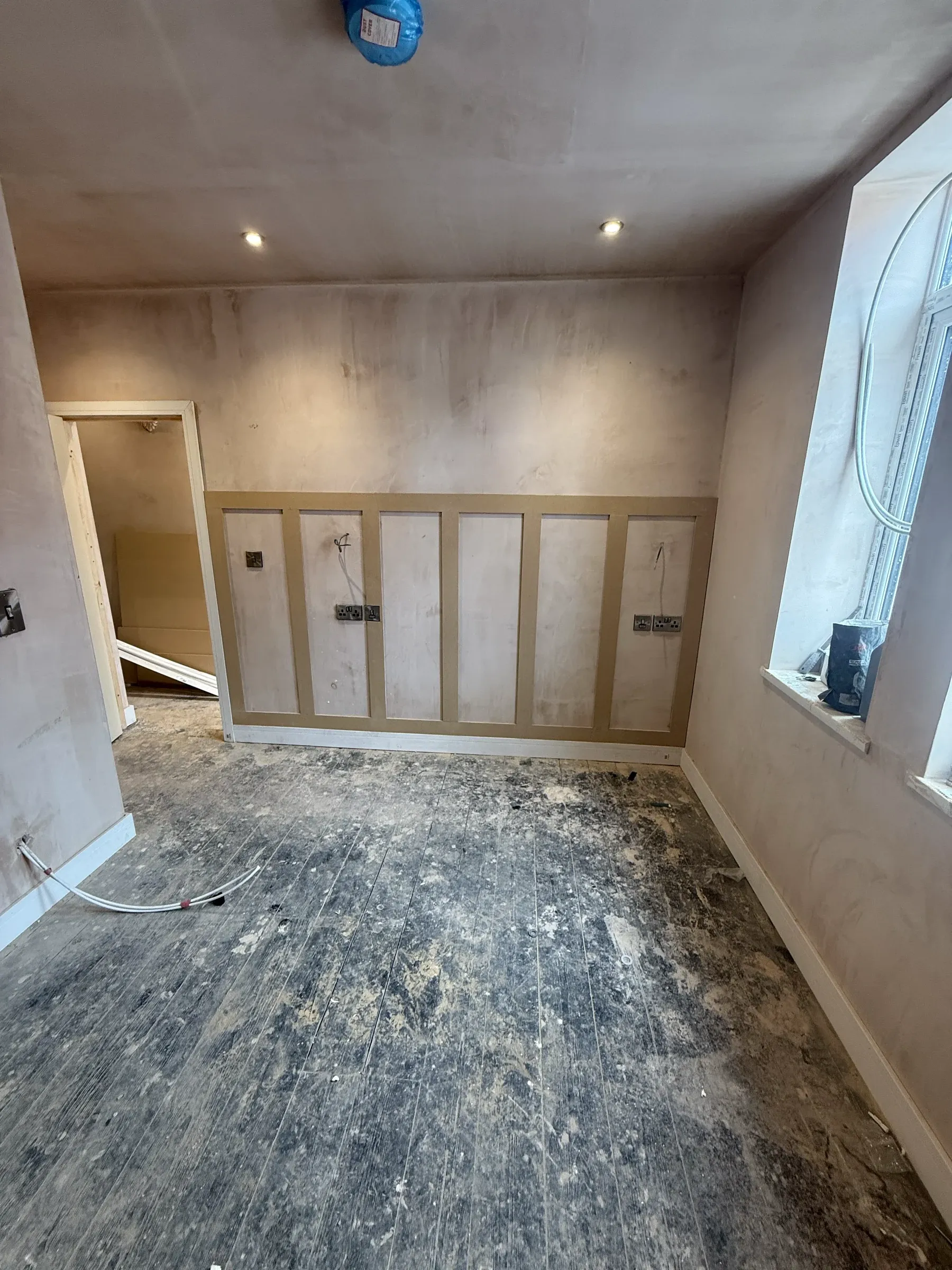 A room at first fix, freshly plastered, with panelling battens fixed and a rooflight overhead