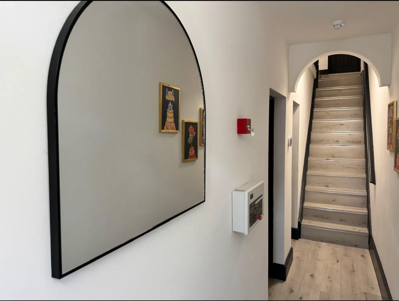 The finished entrance hall, with an arched mirror, wide plank flooring and the staircase beyond