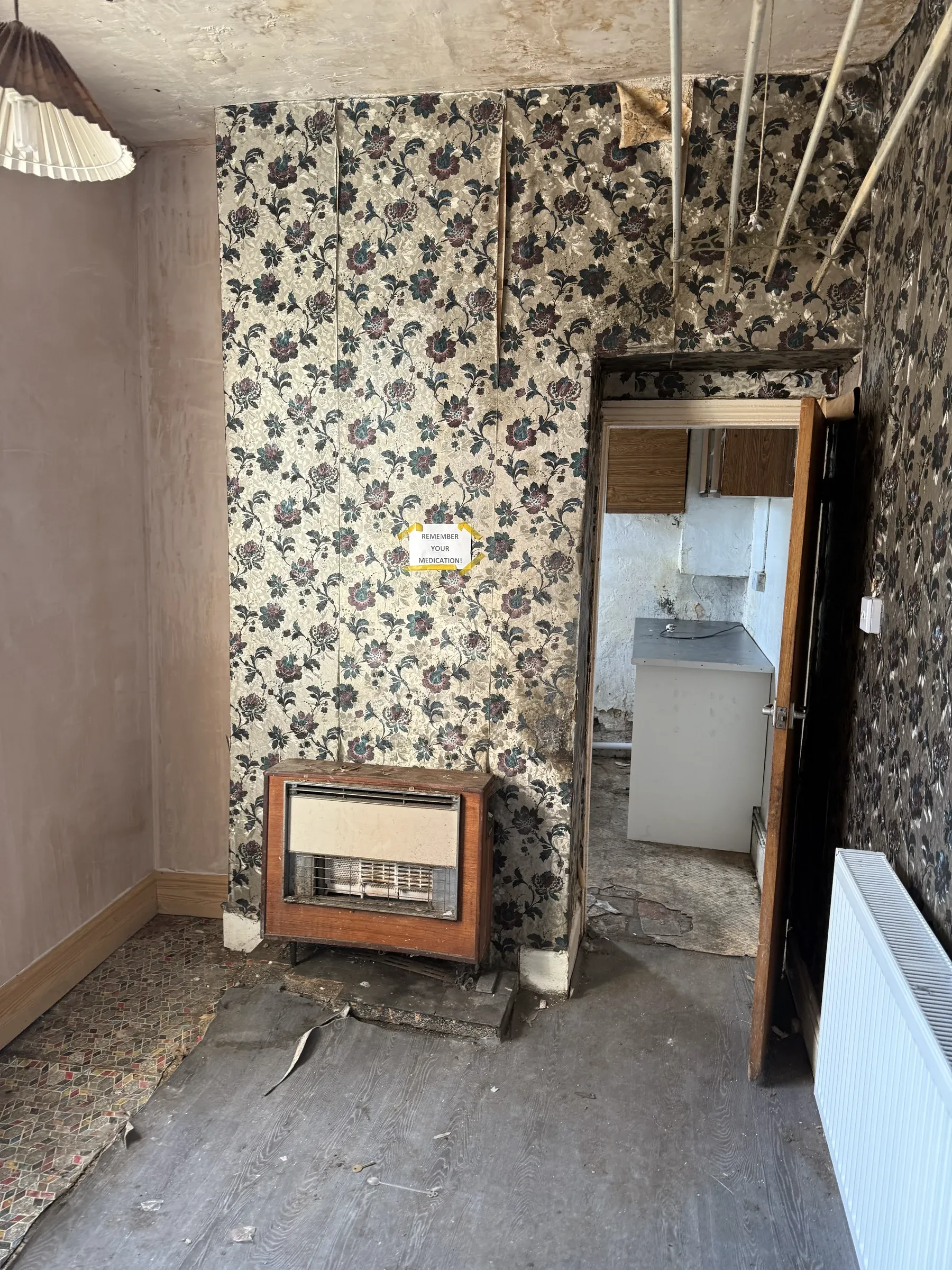 The same room before work started — dark floral wallpaper, an old gas fire and bare floorboards