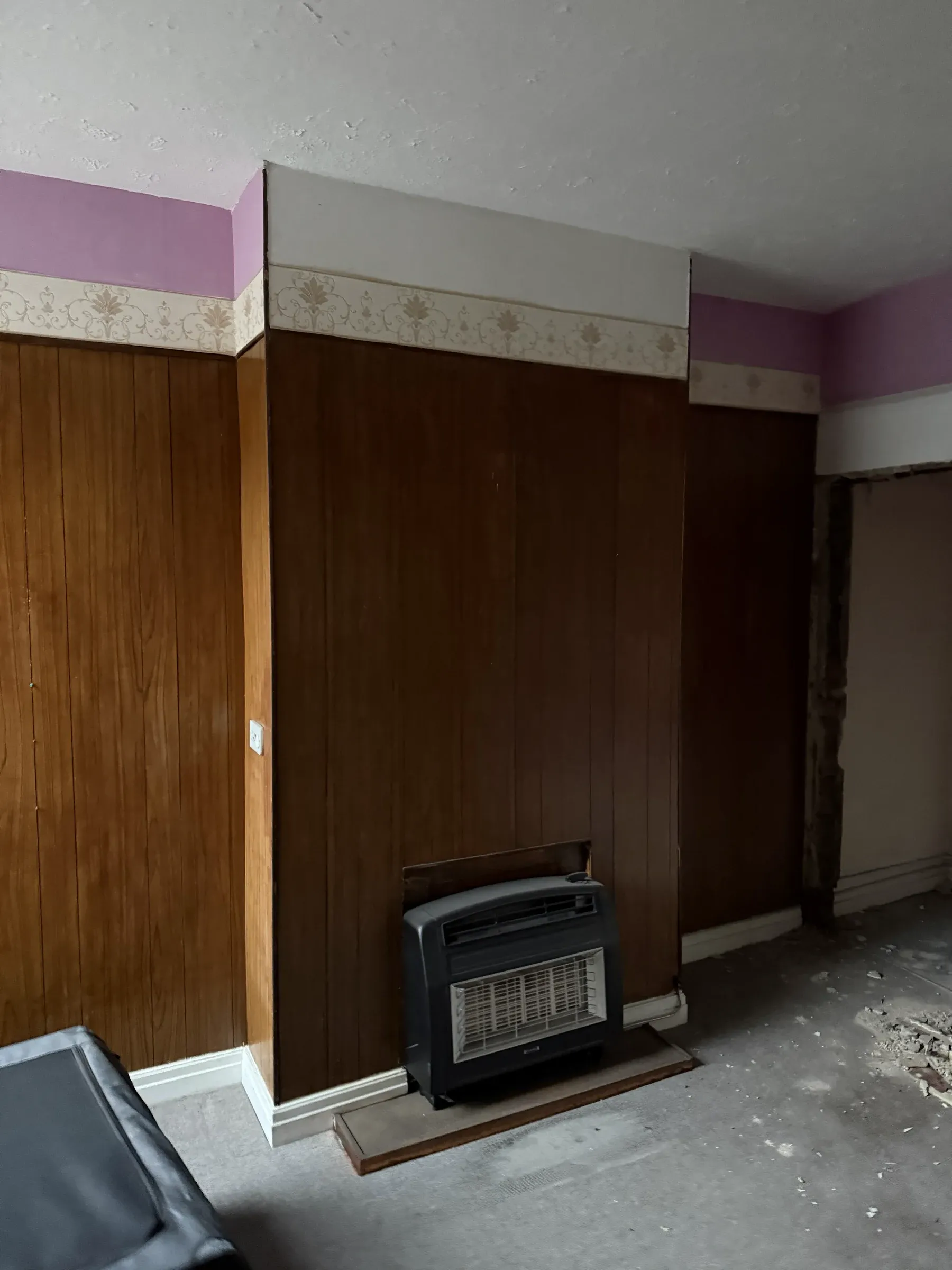 A room before work started, with dark wood panelling to the chimney breast and an old gas fire