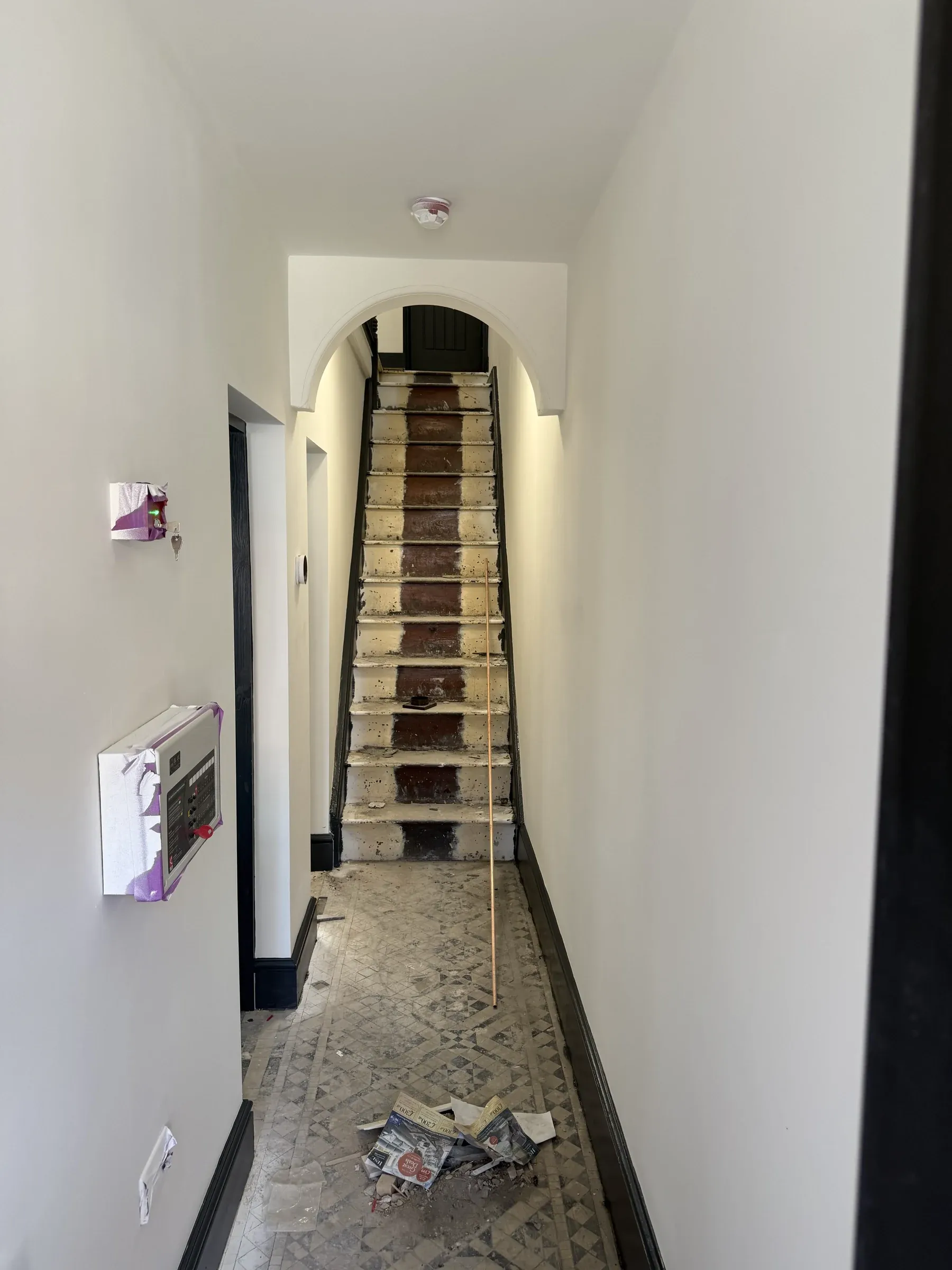 The hallway mid-refurbishment, with the original tiled floor exposed, bare treads and stripped walls