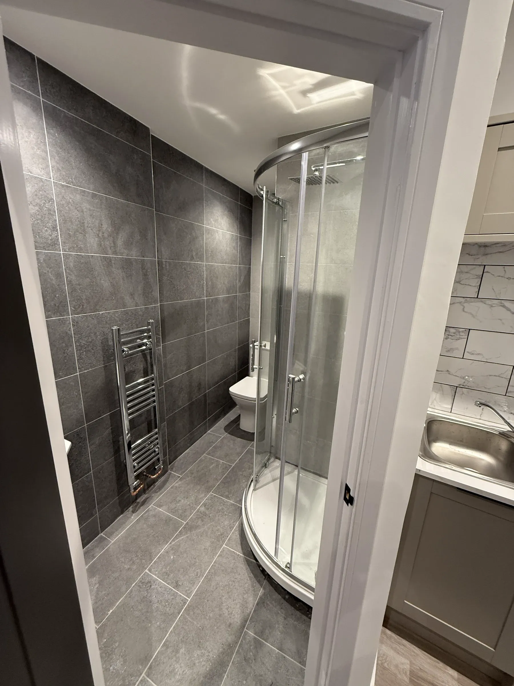 A finished en-suite with a quadrant shower enclosure and large format grey tiling