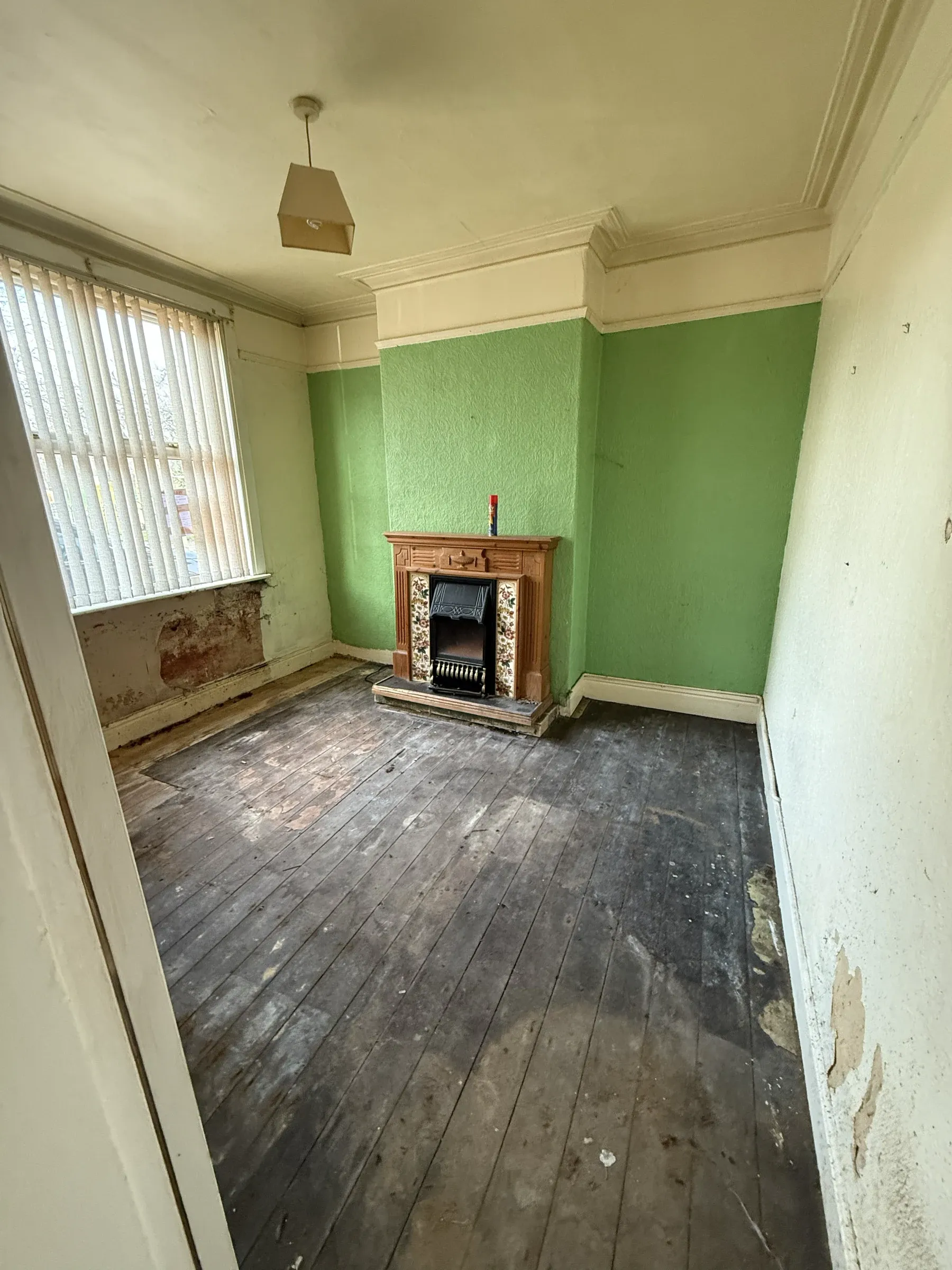 A room stripped back during renovation, with wallpaper coming off, bare floorboards and an original fireplace