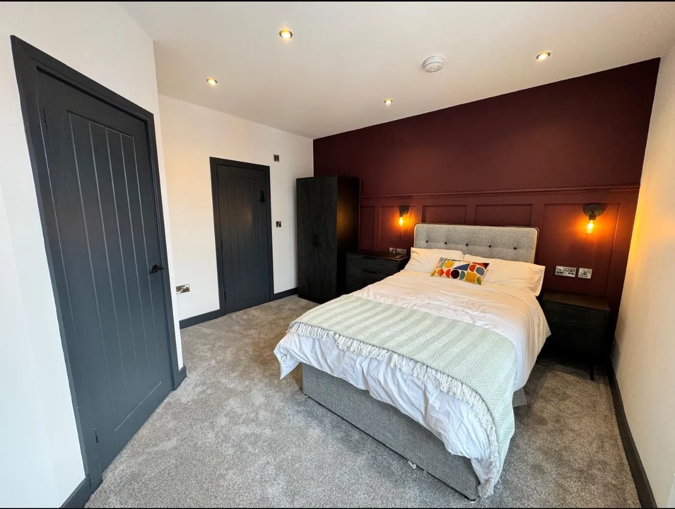The finished bedroom, with a deep burgundy panelled wall, wall lights, a fitted wardrobe and new carpet